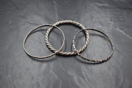 A trio of white metal slave bangles, the two slim moulded bangles being stamped sterling and
