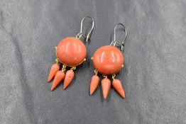 A pair of coral earrings of button form, each having a trio of suspended drops from yellow metal