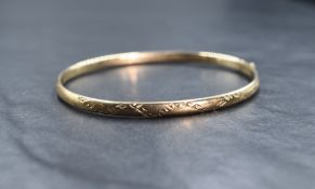 A 9ct gold bangle of narrow hollow form having cut decoration to one side and a concealed clasp with