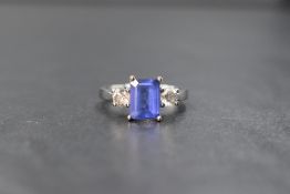 An 18ct white gold tanzanite and diamond three stone ring, the central emerald cut tanzanite measur