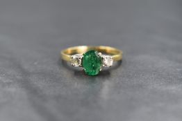 An 18ct gold emerald and diamond set three stone ring, the central oval cut emerald measuring