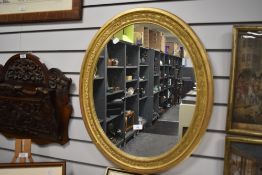 A 20th-century large oval ornate mirror, having a gilt-frame of repeating leaf design, two wall