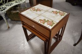 A vintage teak nest of three tables, the top table having frieze drawer and foliate tile top,