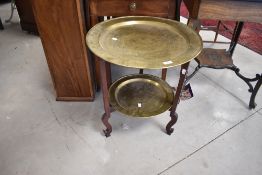 An early to mid 20th Century Oriental folding table having brass top and undertier, diameter approx.