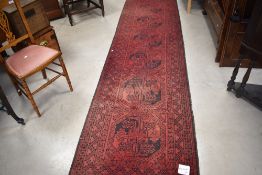 A traditional Turkmen style carpet runner having red ground , some areas of fading and wear but
