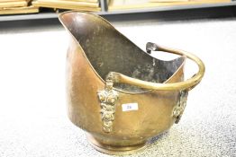 A 19th-century brass and copper helmet coal scuttle, featuring ornately formed handle detailing,