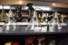 A contemporary trio of clear glass cone pendant lights, having a satin nickel finish and block