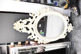 An contemporary resin cream-coloured wall mirror, of oval shape, having ornate decorative floral and