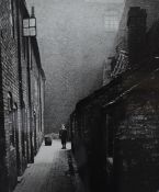 A monochromatic print of a 19th/Early 20th Century photograph, depicting a worker outside of