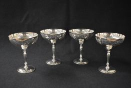 A set of four Elizabeth II silver champagne glasses, having decorative scroll engraving and vacant