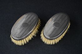 A cased pair of George V silver mounted clothes brushes, of oval form having engine turned