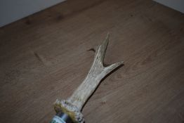 A wooden walking stick with metal feral at each end with an antler mounted on the top to form a