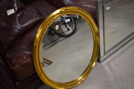 A modern oval gilt framed wall mirror with bevelled plate and moulded decoration 70cm x 58cm