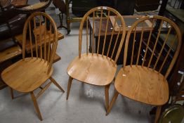 A group of three modern Ercol elm seated stick back chairs, of traditional design with inset