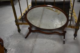 An Edwardian mahogany oval swing dressing mirror, the oval bevelled plate pivoted between shaped