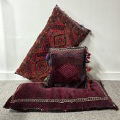 Three carpeted floor cushions in wool, mostly deep red tones with navy accents, each showcasing a