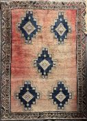 A vintage Iranian wool rug having a light red ground showing signs of wear and sun fading, featuring