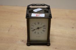 A small early 20th-century French brass carriage clock, with hinged carrying handle above a black