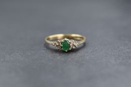 A 9ct gold emerald and diamond set ring, the central oval cut emerald flanked by three round cut