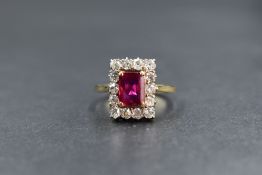 An 18ct gold ruby and diamond set cluster ring, the emerald cut ruby measuring approximately 7mm x