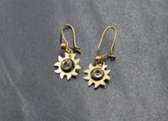 A pair of yellow metal drop earrings, the starburst motif drops having articulated clear paste to