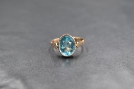 A rose gold blue topaz style ring stamped 9ct having an oval stone in a collared mount with shaped