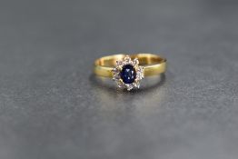 An 18ct gold sapphire and diamond set cluster ring, the oval cut sapphire in a ten round brilliant
