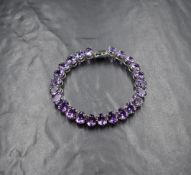 A white metal and amethyst articulated bracelet stamped 375, having twenty four oval amethysts in