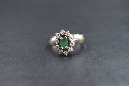 A white metal emerald and diamond cluster ring stamped 18ct having an oval emerald, approx 0.5ct
