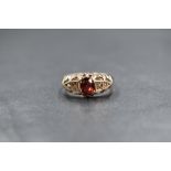 A yellow metal presumed gold garnet and pearl set ring, the central oval cut garnet flanked by two