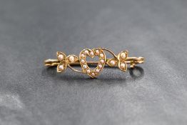 A yellow metal presumed gold, seed pearl set bar brooch, the central openwork heart motif with