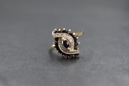 A 9ct gold diamond and sapphire ring having a small central marquise cut sapphire within a swirl