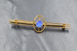 A yellow metal presumed gold opal set bar brooch, the central bezel set opal in an openwork bar