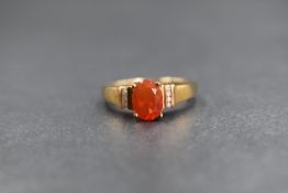 A 9ct gold fire opal ring having a central oval opal in a raised four claw mount flanked each side
