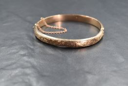 A 9ct gold hinged bangle, having decorative engraving with safety chain, marked 375, 10g. Damage