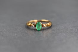 A 9ct gold emerald ring having a small oval emerald flanked by two diamond chips to twist