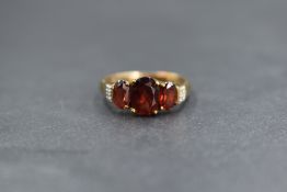 A 9ct gold garnet trilogy ring having three claw set oval garnets flanked by diamond chip set