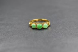 A 14ct gold jade ring having three claw set graduated jade cabochons to split shoulders having