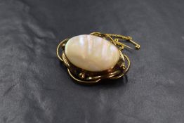 A yellow metal mother-of-pearl set brooch, the oval bezel set mother-of-pearl in a decorative