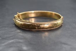 A 9ct gold hinged bangle, the bangle having decorative scroll engraving with twisted rope motif