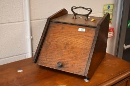 An early 20th century oak coal scuttle, with typical hinged and sloped from, lacking liner, rear