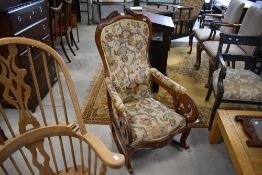 A Victorian design upholstered mahogany rocking chair, the shaped and carved crest over the shaped