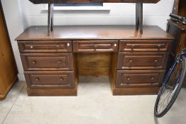 A modern reproduction stained wood desk, having an arrangement of seven drawers around a central