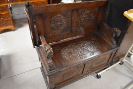 A reproduction carved oak Monk's bench, of traditional design with pivoted top/back scroll carved