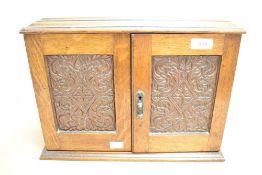 A late 19th to early 20th-century Arts and Crafts-style oak smokers cabinet, having twin floral