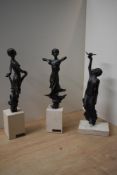 A group of three patinated metal figurines, depicting themes of movement and grace, raised and