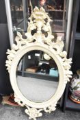 A contemporary resin cream-coloured wall mirror, of oval shape, having ornate decorative floral and
