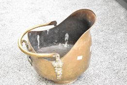 A 19th-century brass and copper helmet coal scuttle, featuring ornately formed handle detailing,