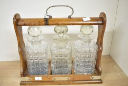 A Victorian oak three-bottle tantalus, having white metal mounts and three crystal-cut glass
