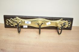 An early 20th-century brass wall-mounted coat rack, featuring scrollwork fittings upon a dark